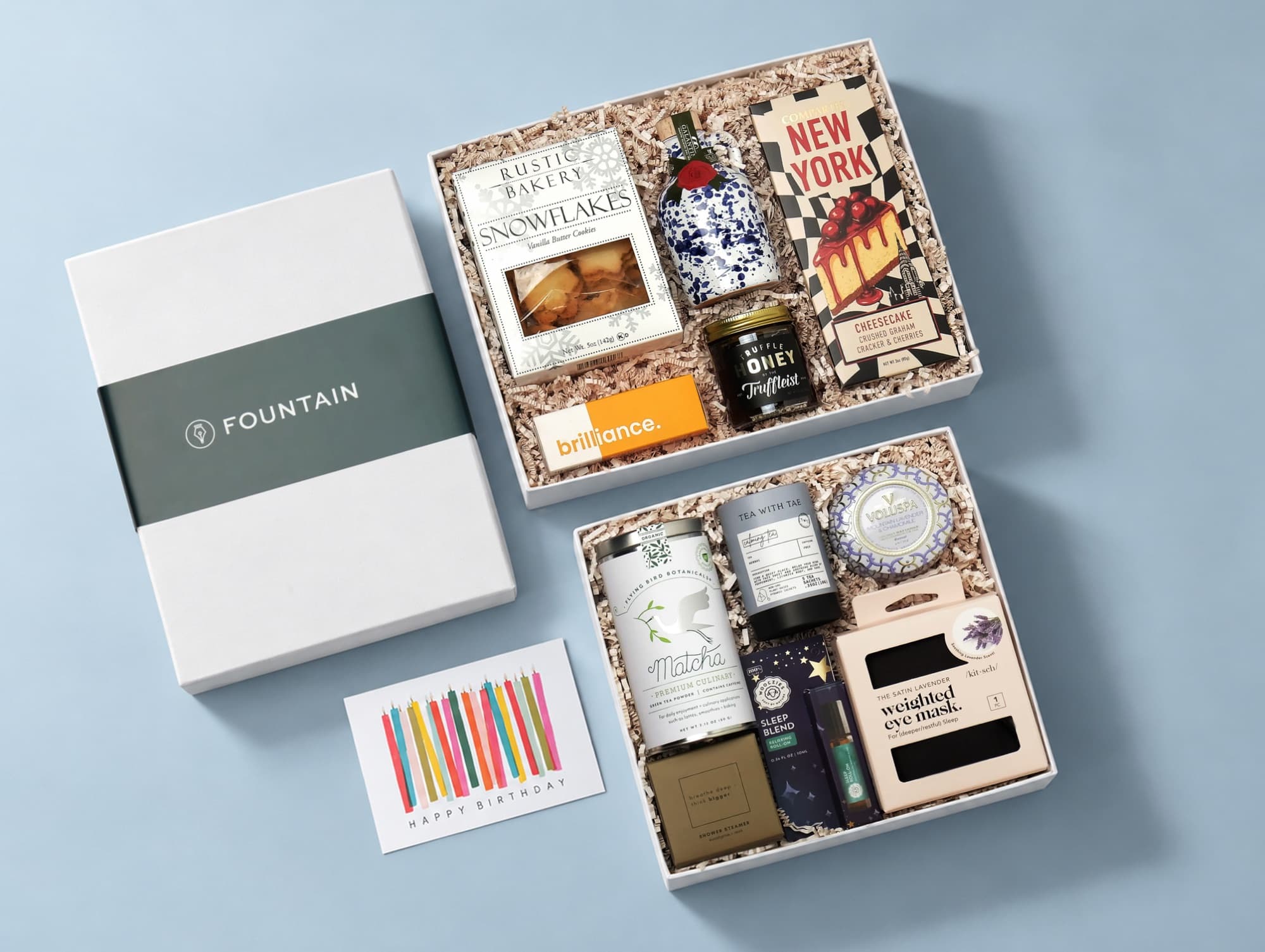 A Fountain box with its green band beside two open gift boxes of treats and a birthday card